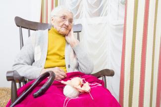 Elderly lady sitting in rocking chair with cane and knitting