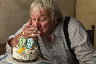 Elderly man lighting a cigarette with a candle on birthday cake