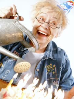 Elderly woman pouring water out of a watering can over birthday candles