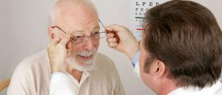 Optometrist putting glasses on senior man