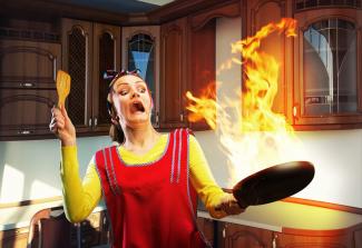 Woman holding at pan on fire in the kitchen