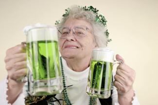 Elderly woman celebrating St. Patrick's Day with 2 mugs of green beer