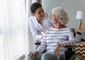 Smiling elderly woman in wheelchair talking to caregiver