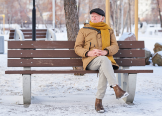 Senior man out for a winter walk, taking a break on a bench