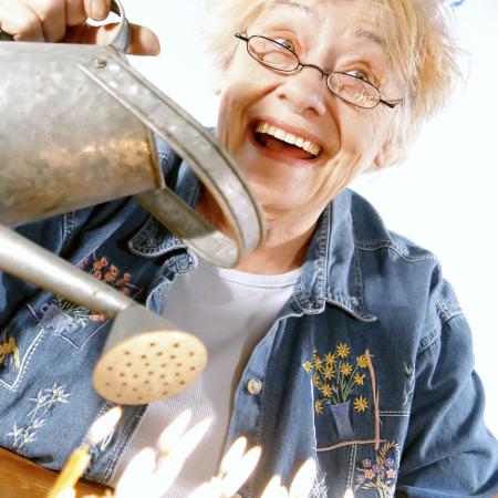 Elderly woman pouring water out of a watering can over birthday candles