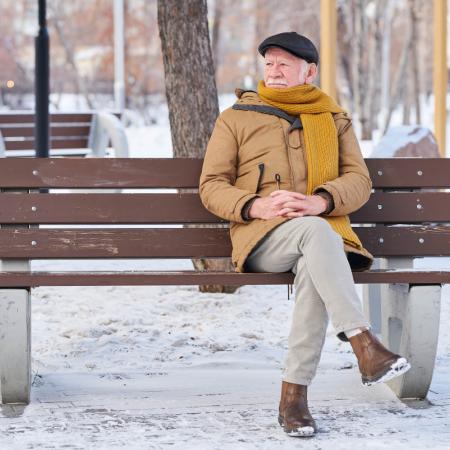 Senior man out for a winter walk, taking a break on a bench