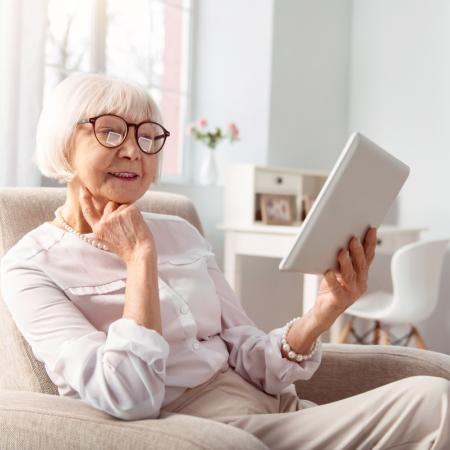 Senior woman reading a book on her tablet indoors during the winter